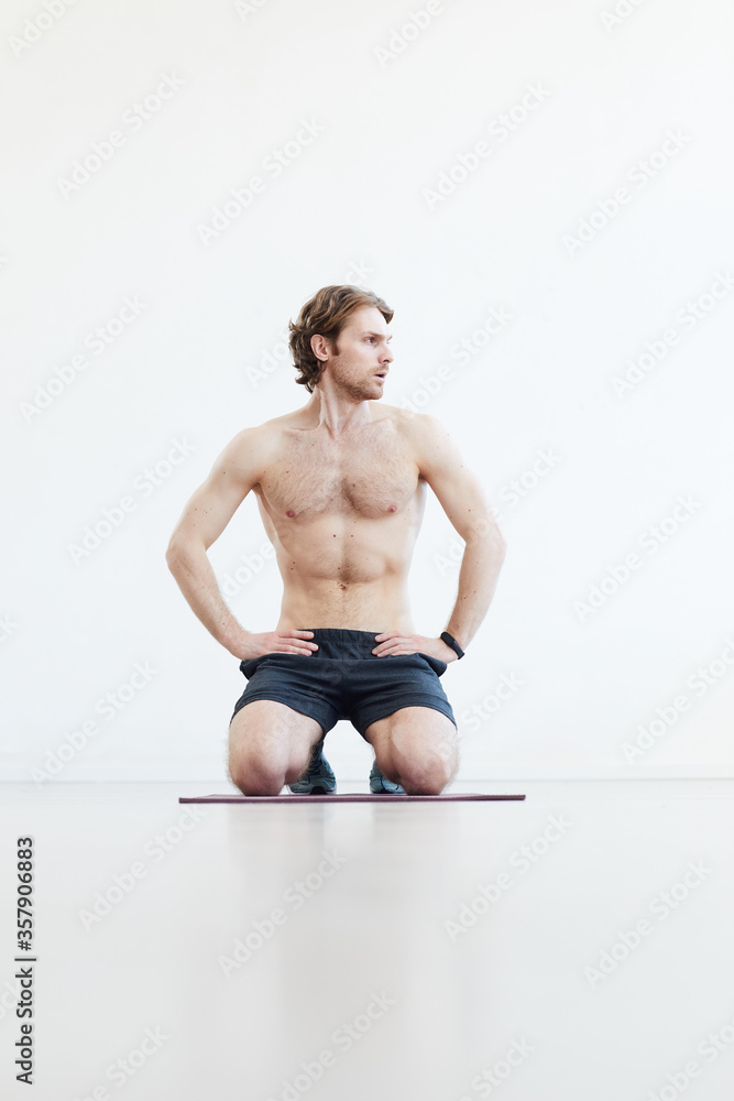 Obraz premium Young muscular man sitting on the floor and resting after training against the white background