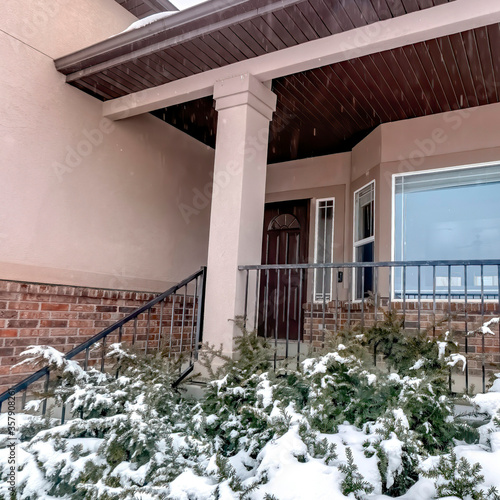 Square Snowy evergreens at the yard of brick home with bay window and front porch photo