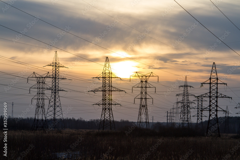 High voltage power lines in the middle of a field at sunset. Industrialization. Electrification. Power supply.