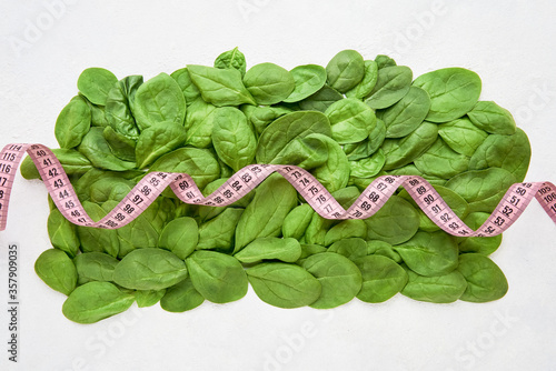 Green spinach leaves with pink tape measure. Healthy food, dietary and weight lose concept. Top view, copy space.