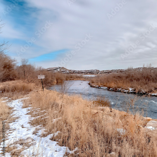 Square crop River with flowing water along grassy and rocky banks dusted with winter snow