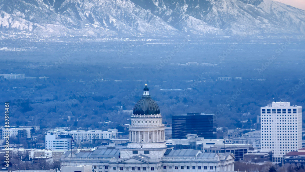 Panorama Utah State Capital Building against steep snowy mountain and gray cloudy sky