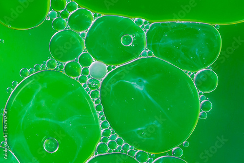 Green background with plastic oil bubbles on water surface with smoke pattern