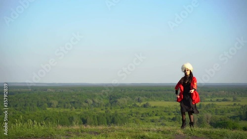 Georgian girl in white papakha and red national dress dances national dance named: rachuli, acharuli, osuri, shalaxo, mtiuluri. on the green hills of Georgia background. Georgian culture lifestyle. photo