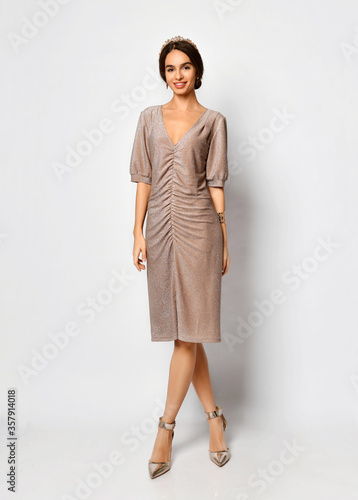 Young pretty lady in draped powder-pink sequined dress and tender diadem on hair looking pleasantly surprised. Full length portrait isolated on white