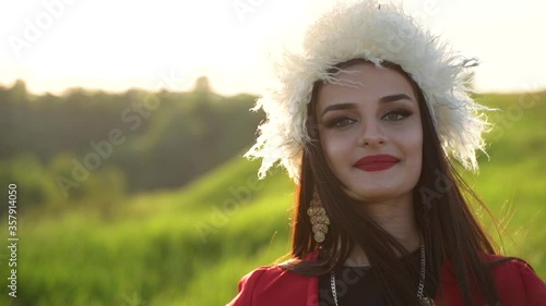 Georgian girl in white papakha and red national dress walks and smiles on the green field. Video portrait. Georgian culture lifestyle. photo