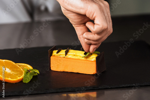 Chef hands decorate orange cake. Closeup hands decorate dessert with chocolate.