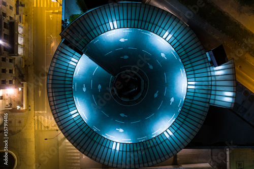 Top down view of a round blue parking garage at night
