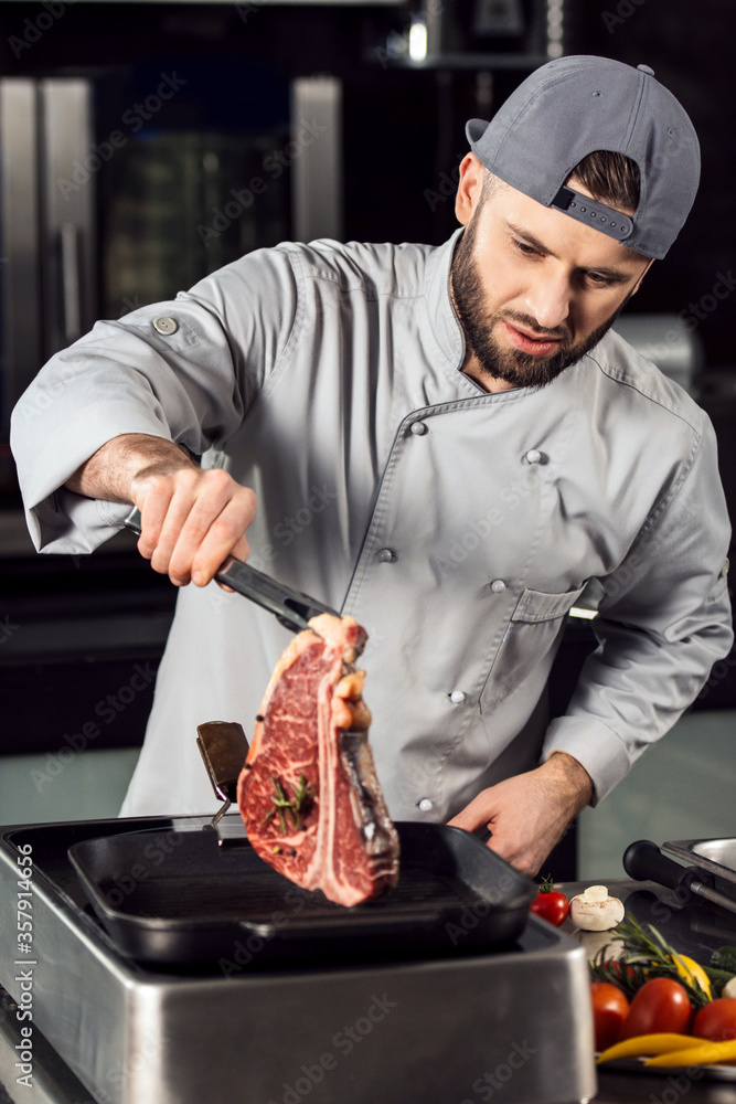 Chef put steak on griddle pan. Chef male cook fresh beef at kitchen restaurant.
