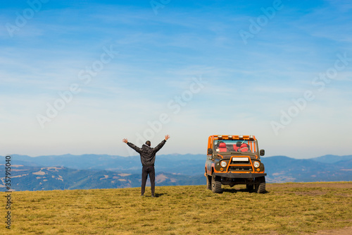 Happy man with hands up travel by car on mountains top.