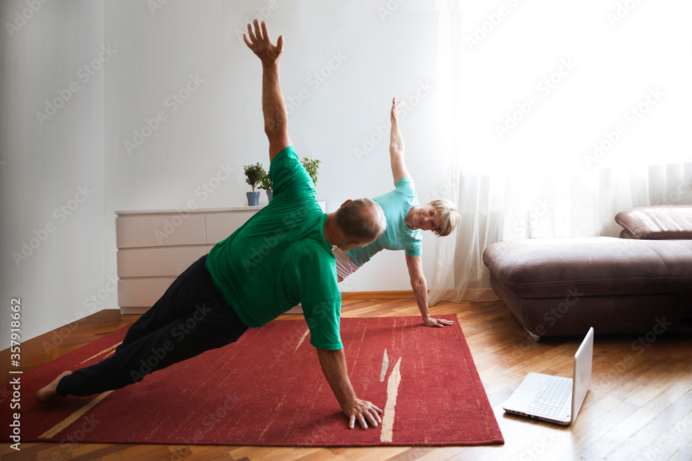 active senior couple doing stretching exercise and watching online workout  tutorials on the laptop in living room at home. home fitness, activewear.  Stock 写真 | Adobe Stock