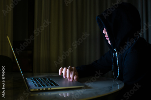 Hacker is  hacking into the computer network. Young boy in a dark room with laptop.  Hacker with a laptop.