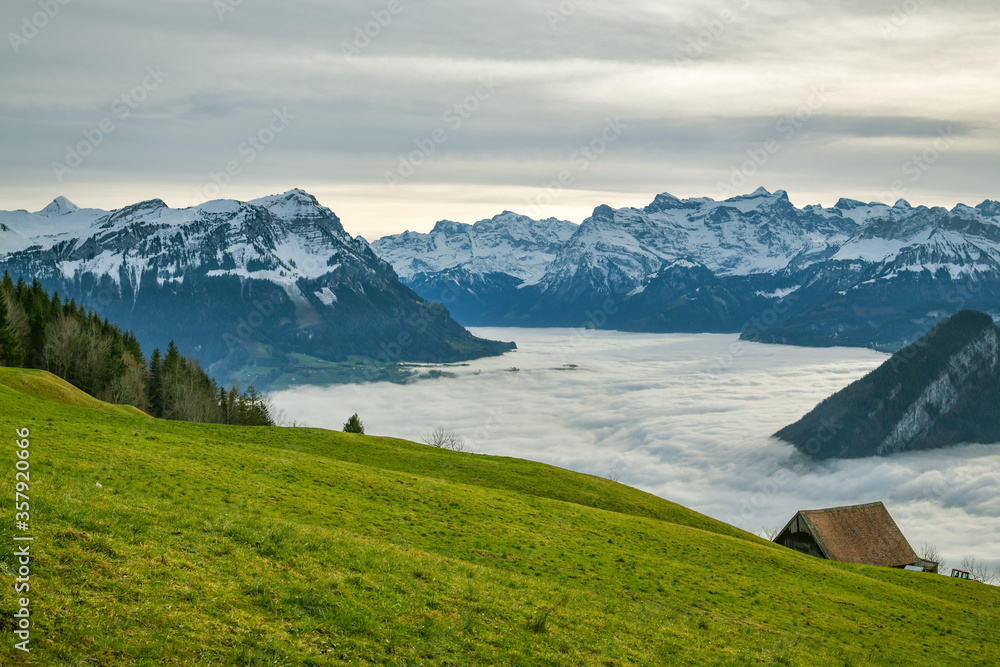 Clouds covering lakes below majestic Alpine peaks as seen from small meadow above the Sattel