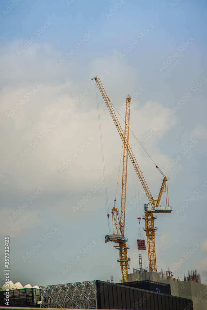 Long tower crane at large scale construction site. Skyscraper building construction with the tower cranes on top under the dramatic sky background.