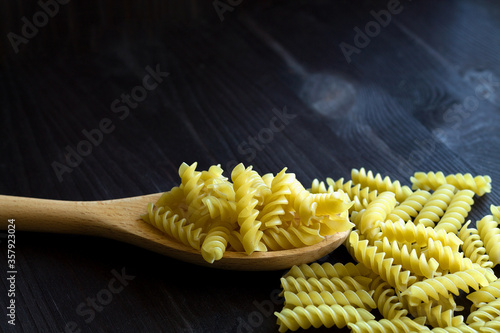raw pasta on wooden background. Fusilli pasta on wooden table. uncooked pasta on black with copy space. Italian Cuisine.