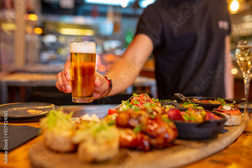 waiter serving beer at a Spanish restaurant with a table full of tapas photo