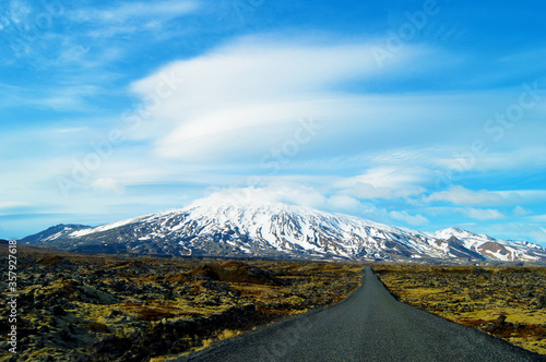 Snowy mountains, volcanic land, meadow, amazing clouds and a lonely path