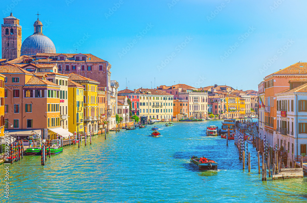 Venice cityscape with Grand Canal waterway. Boats, yachts, vaporettos docked and sailing Canal Grande. Venetian architecture buildings, blue clear sky background in summer day, Veneto Region, Italy