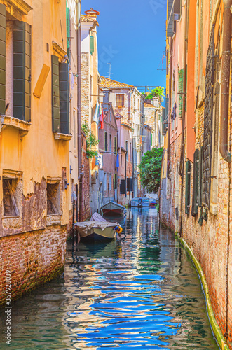 Venice cityscape with narrow water canal with boats moored between old colorful buildings, Veneto Region, Northern Italy. Typical Venetian view, vertical view, blue sky background