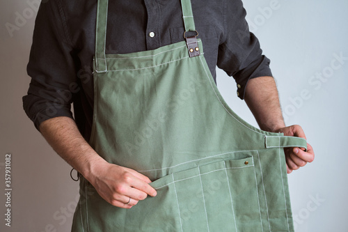 A man in a kitchen apron. Chef work in the cuisine. Cook in uniform, protection apparel. Job in food service. Professional culinary. Green fabric apron, casual stylish clothing. Handsome baker posing photo