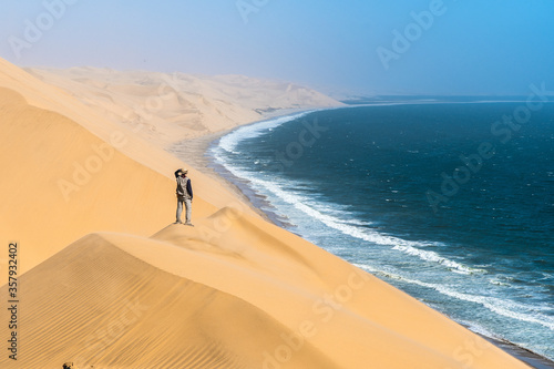 Fototapeta Naklejka Na Ścianę i Meble -  Tourist admiring the view from a sand dune at Sandwich Harbour