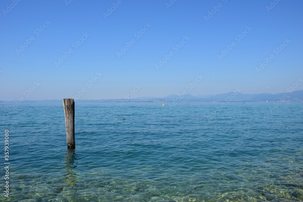 Fototapeta premium Holzpfahl im Wasser als Anlegestelle für Boote und Schiffe am Gardasee in den Sommermonaten 