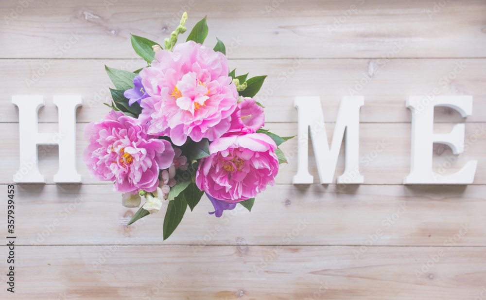 Letters HOME and  bouquet with pink peonies on a wooden table