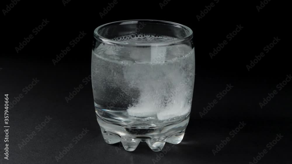 Two effervescent tablets dissolved in a glass of water. Black background. Two effervescent tablets dissolved in a glass of water. Black background.