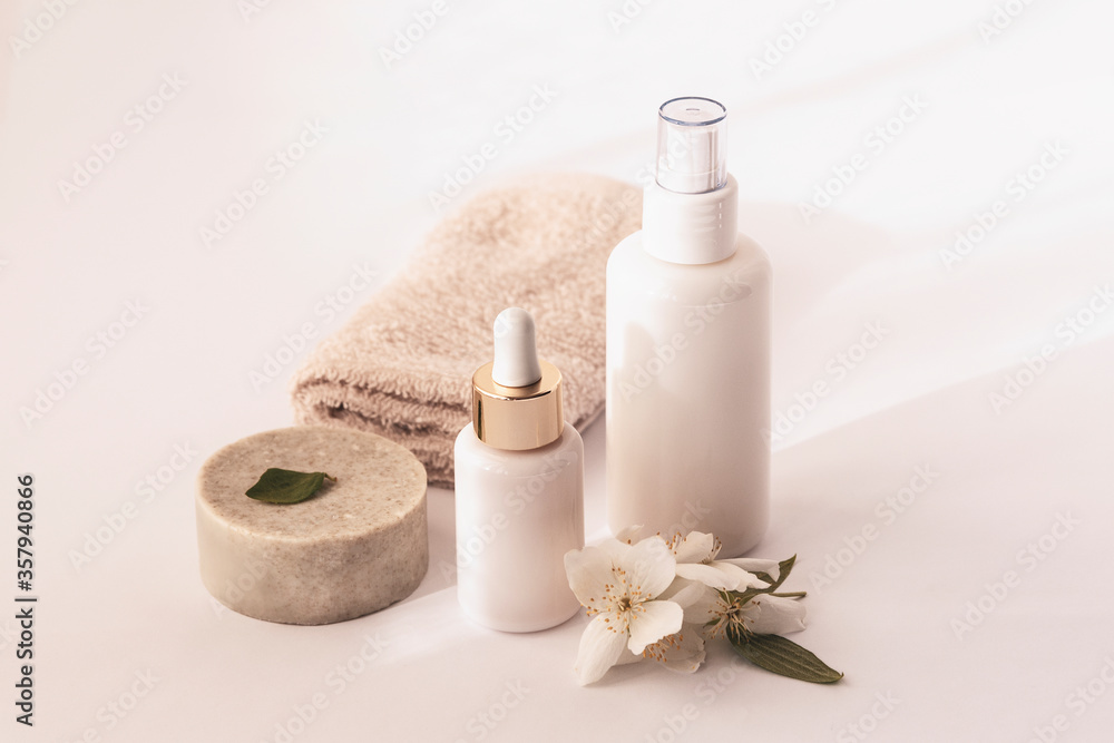 Cosmetic soap, serum and tonic bottles in white blank packages with jasmine blossom, white background, copy space
