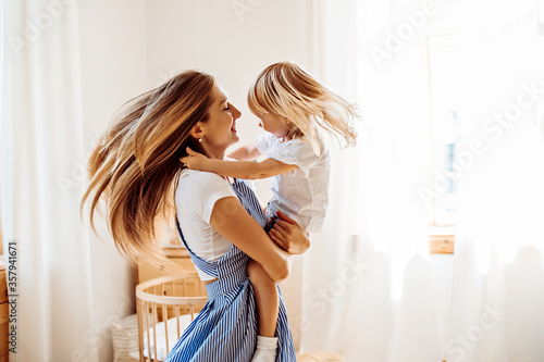 Young mother or babysitter with a little girl in her arms spin in the middle of the room photo
