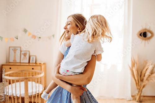 Young mother or babysitter with a little girl in her arms spin in the middle of the room