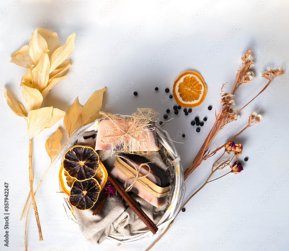 A handmade soaps brown-pink color with an orange tint and dried slices of oranges, roses flowers and spikes of dried leaves and berries on a white background with wooden texture .The concept of