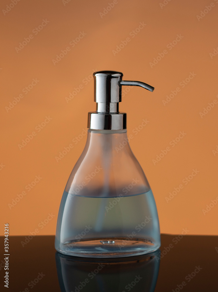 Bottle of liquid soap glass dispenser on orange/yellow background reflecting on dark surface Bottle of liquid soap glass dispenser on orange/yellow background reflecting on dark surface