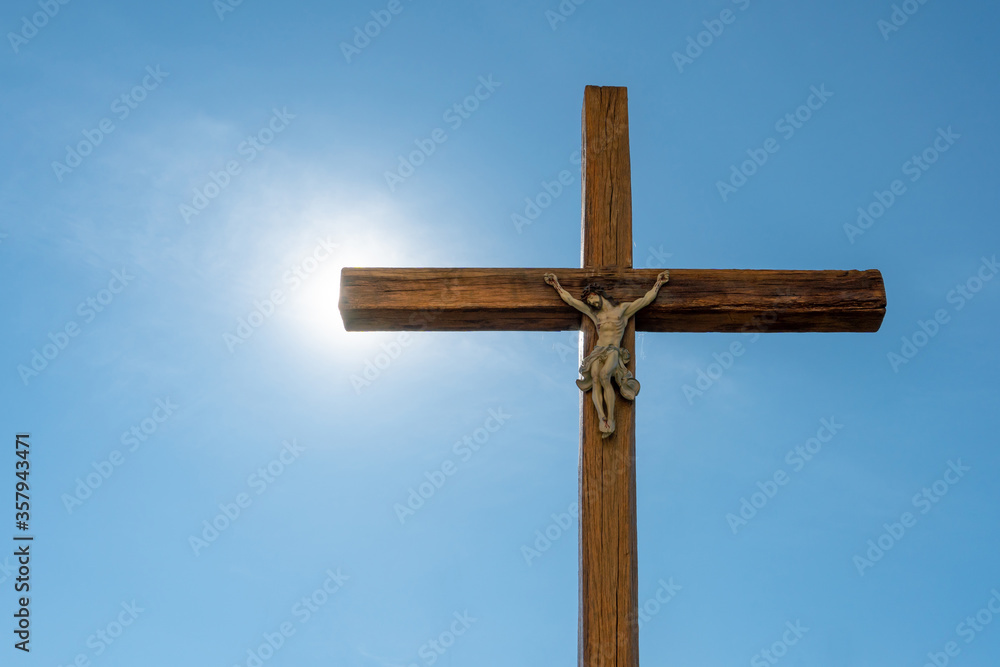 An old wooden Catholic cross against the background of the sun and clear blue sky. Religion and service to God as a path to redemption from sin. The face of Jesus crucified on the cross.