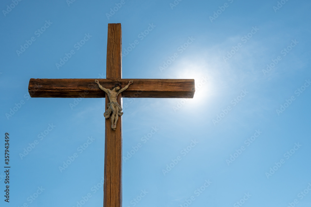 An old wooden Catholic cross against the background of the sun and clear blue sky. Religion and service to God as a path to redemption from sin. The face of Jesus crucified on the cross. An old wooden Catholic cross against the background of the sun and clear blue sky. Religion and service to God as a path to redemption from sin. The face of Jesus crucified on the cross.