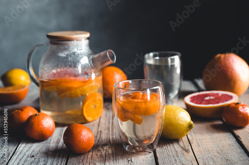 Citrus tea in a transparent teapot on a table with grapefruit and on a wooden table. Healthy drink.