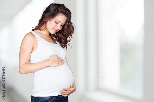 A pregnant young woman in white t-shirt on bright background
