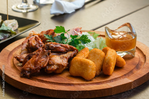 Plate with appetizers of chicken, nuggets and meat rolls with sauce on a wooden plate
