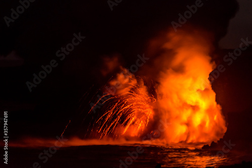 Lava flow from Big Island in Hawai'i into the Pacific Ocean glowing bright yellow, orange, and red with a explosion photo