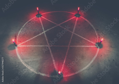 White pentagram symbol on concrete ground. Illuminated with candles. Dark background. Scary, mystical occultism.