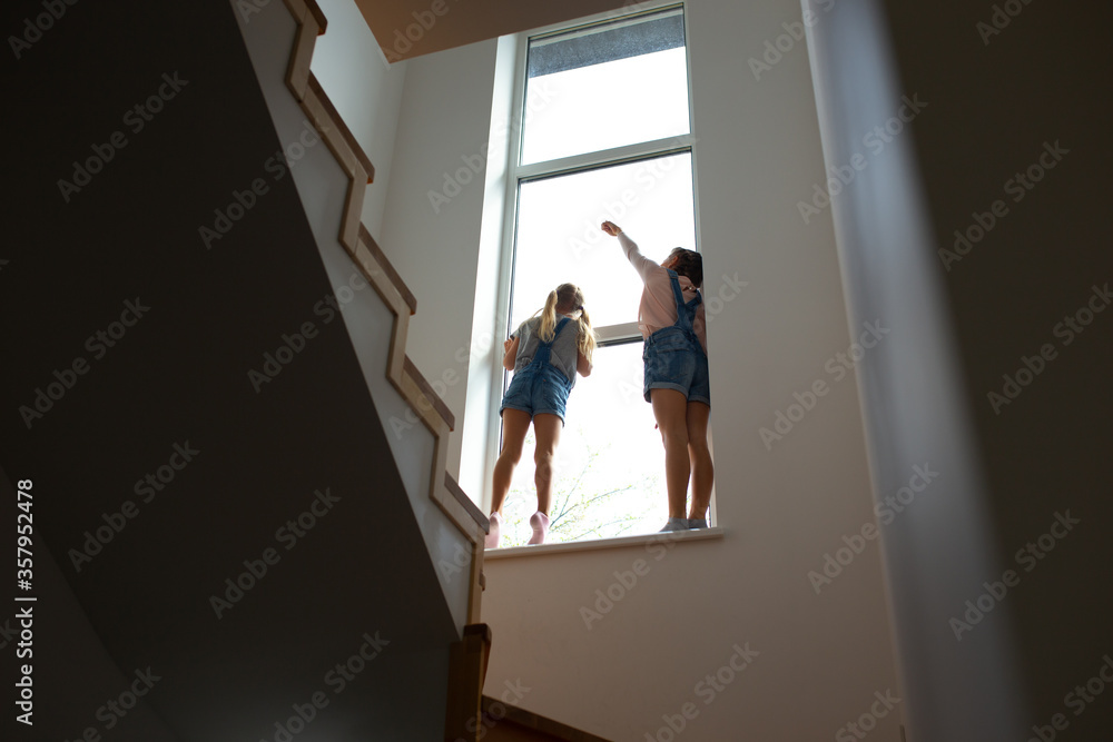 Two little girls standing on windowsill near stairs