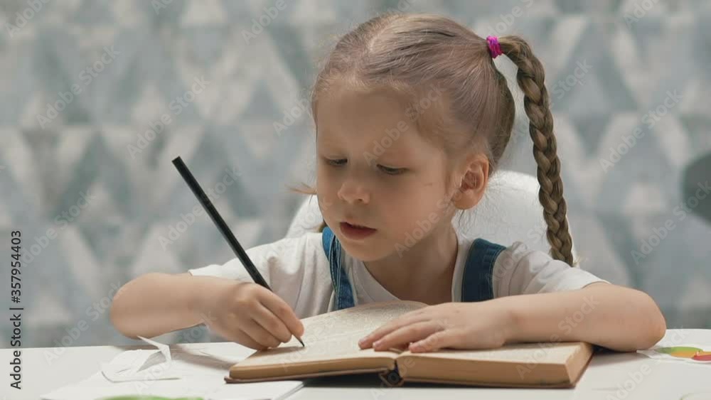 closeup slow motion portrait of little girl with perky pigtails, sitting at table, reading book at home, emphasizes pencil lines closeup slow motion portrait of little girl with perky pigtails, sitting at table, reading book at home, emphasizes pencil lines