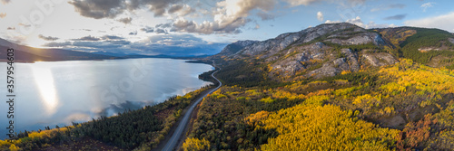 Stunning fall autumn landscape in northern Canada, Yukon Territory. Taken by drone on the side of a lake with mountains and road. 