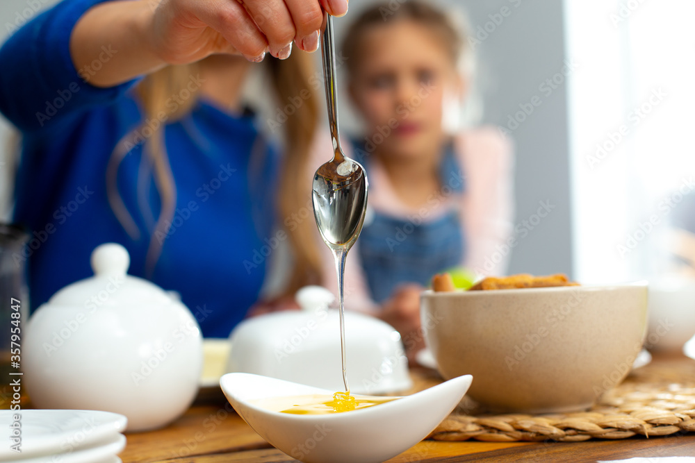 Young woman holding teaspoon with dripping honey