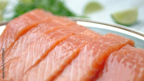 Close-up slow-motion of sliced fresh raw red salmon.
Raw salmon in a silver plate on the wooden table with lemon and herbs/greens ingredients on the side. Concept of healthy seafood. Salmon in 4K.