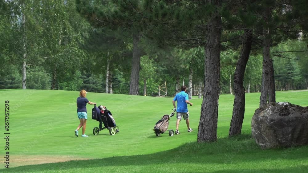 Players golfers walking on perfect golf course at summer day pushing an equipment carts, slow motion Players golfers walking on perfect golf course at summer day pushing an equipment carts, slow motion