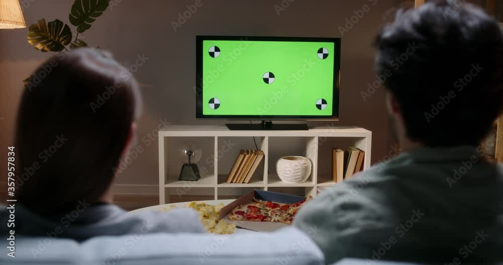Unrecognizable couple sitting together on couch at home, watching tv shows with chroma-key green screen and eating unhealthy food 4k footage template Unrecognizable couple sitting together on couch at home, watching tv shows with chroma-key green screen and eating unhealthy food 4k footage template