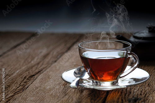 A glass of hot organic teacup with saucer, spoon and kettle on wooden table background. 