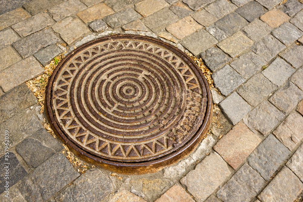 An iron manhole from a well against the background of a road made of stone paving stones. Street, road surface.