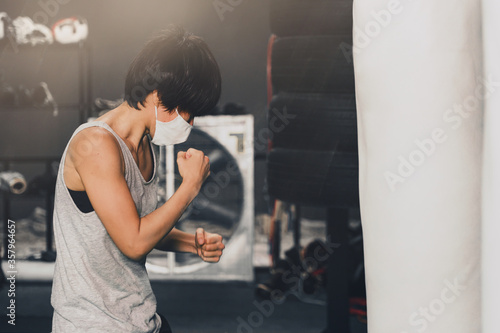 woman wearing medical mask training boxing with punching bag in gym